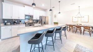 A modern kitchen with white cabinets, a large island with bar stools, stainless steel appliances, and pendant lighting. - Beautiful Storey Lake Retreat, Minutes from Disney (Kissimmee)