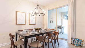 A dining area with a table set for six, surrounded by six chairs, a chandelier, and framed artwork on the wall. - Beautiful Storey Lake Retreat, Minutes from Disney (Kissimmee)
