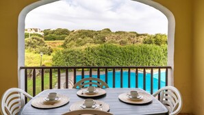 A balcony with a table set for two, overlooking a swimming pool and lush greenery.
