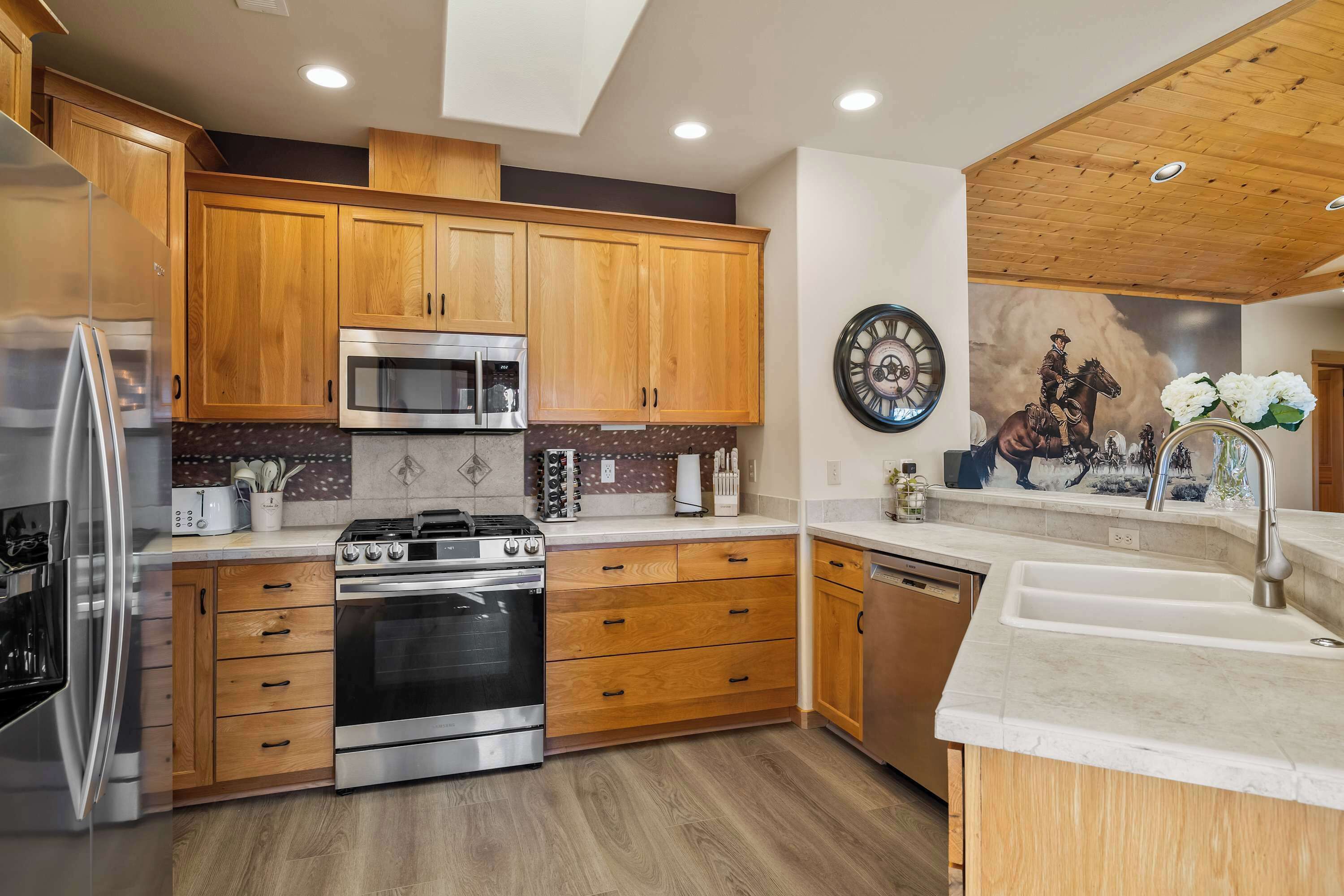 A modern kitchen with wooden cabinets, stainless steel appliances, and a decorative clock.