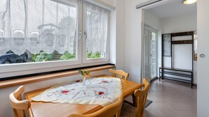 A dining area with a table set for four, a window with sheer curtains, and a view of greenery outside.