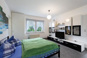 A modern bedroom with a bed, a TV, and a window with a view of greenery.