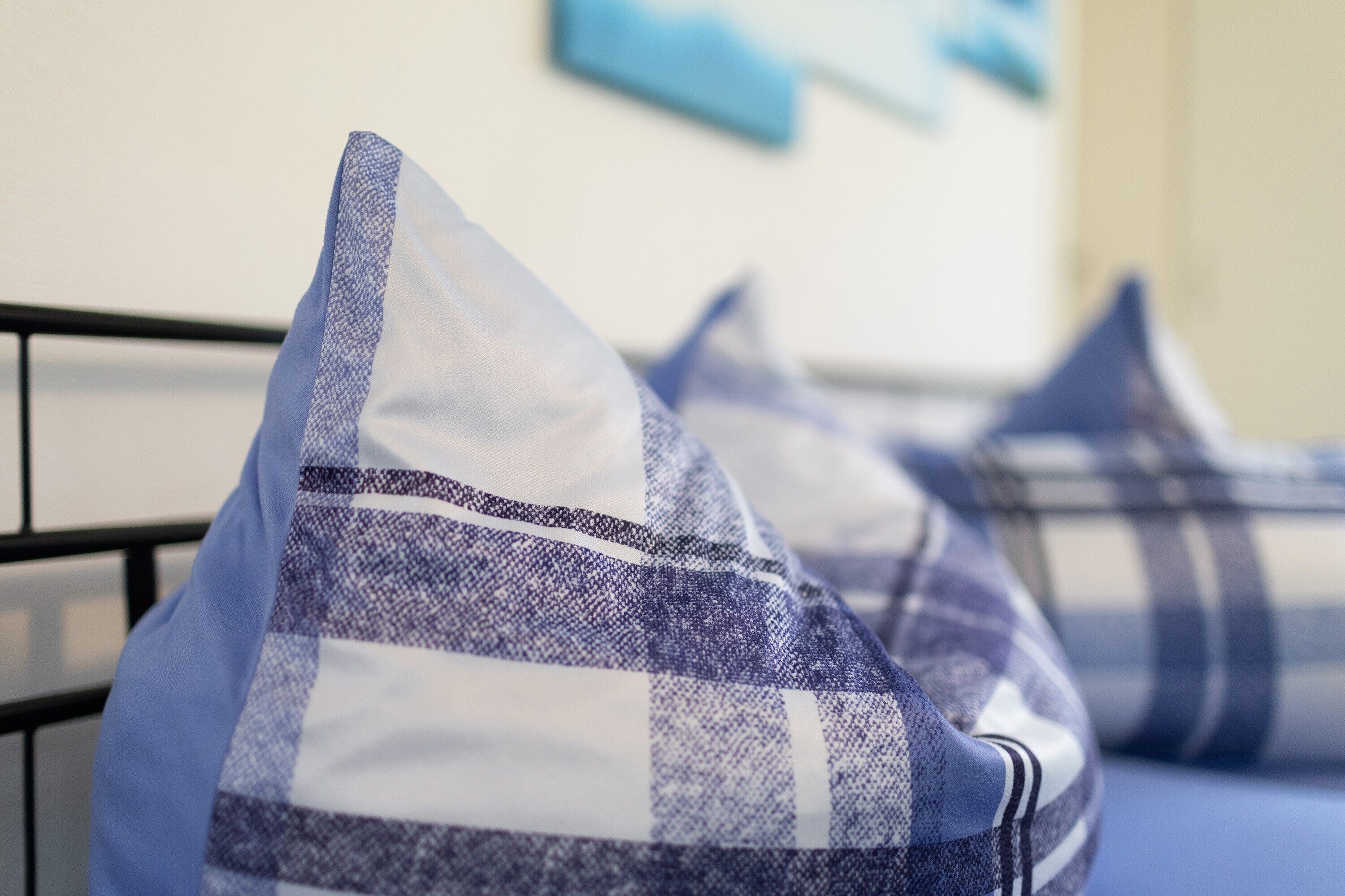 A close-up of a bed with a metal frame and blue and white checkered pillows.