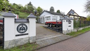 A gated entrance with a sign, a red vehicle, and a white building with a grey roof.