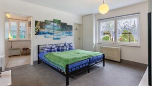 A bedroom with a bed, a radiator, a window with curtains, a door, and a wall with a waterfall painting.