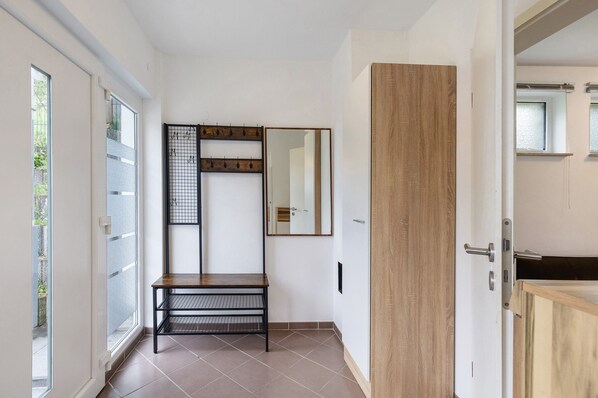A hallway with a bench, a wooden door, a mirror, and a window.