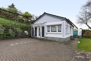 A single-story house with a brick driveway, a wooden pergola, and a stone wall.