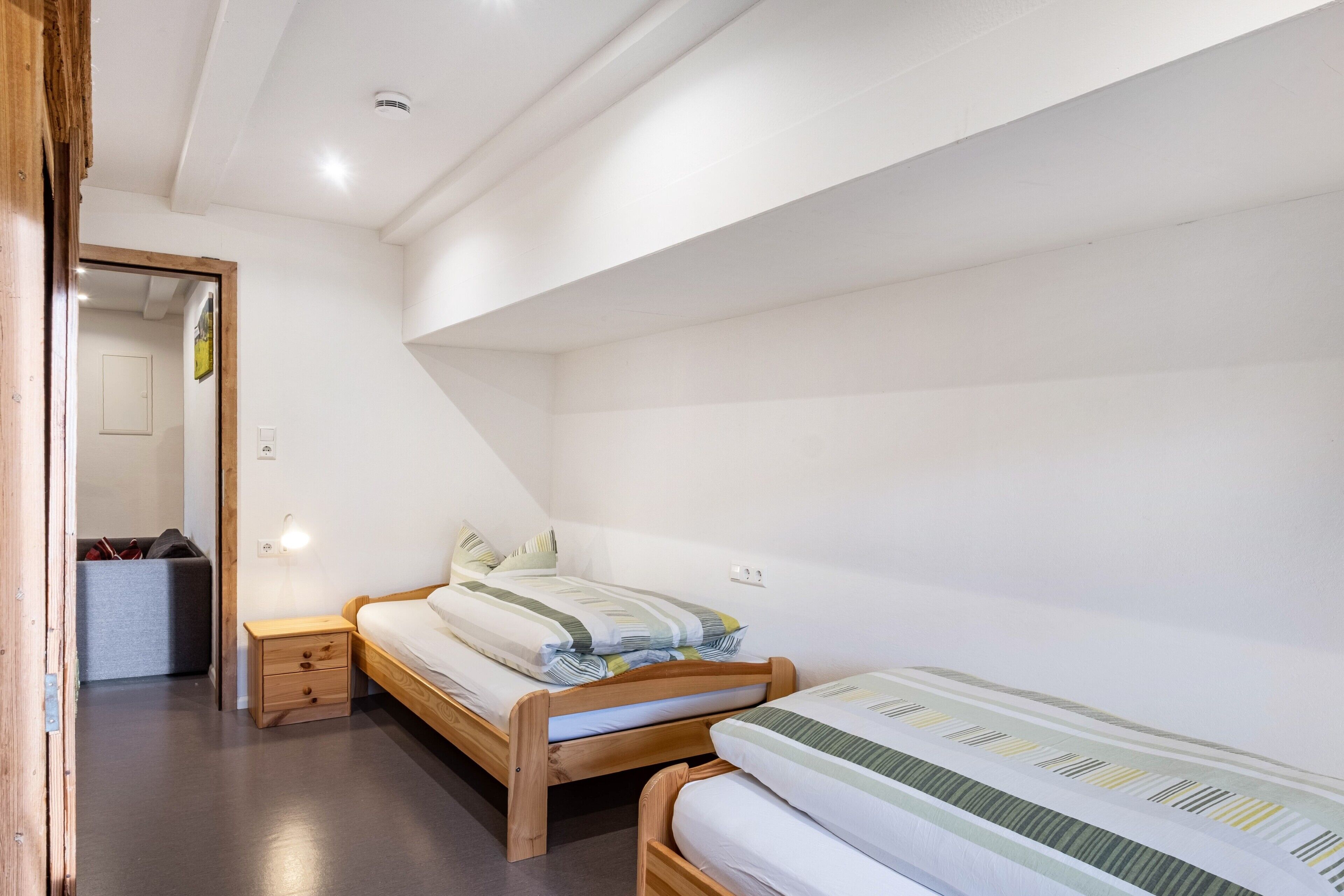 A bedroom with two wooden beds, a small bedside table, and a mirror.
