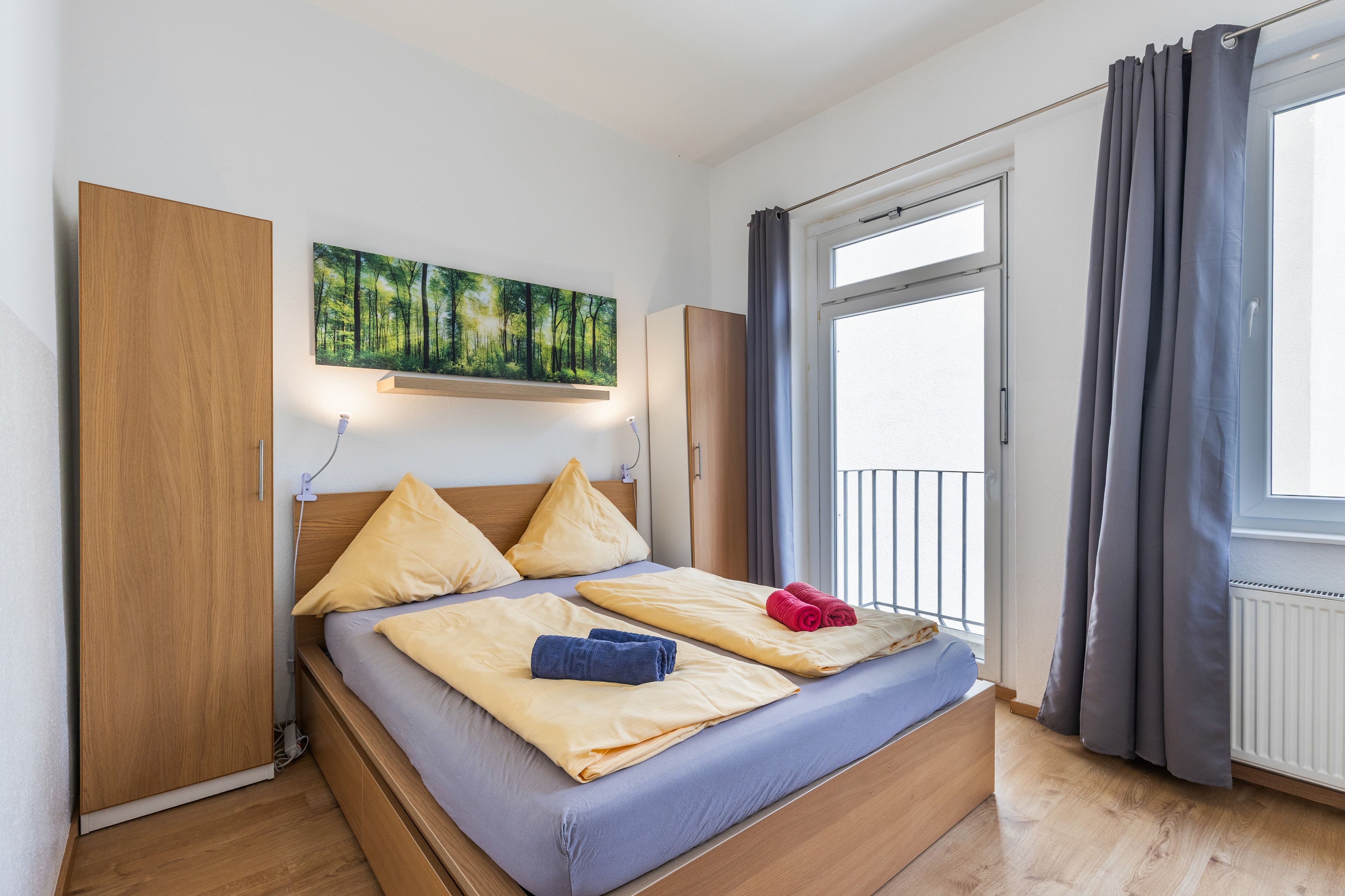 Une chambre à coucher avec un lit, un tableau, une armoire et une fenêtre avec des rideaux.