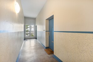 Ein Flur mit einer blauen Tür, einem Fenster und einer Leuchte.