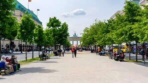 A public square with benches, trees, and a prominent building in the background.