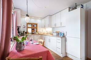 A modern kitchen with white cabinets, a red and white checkered tablecloth, and a hanging light fixture.