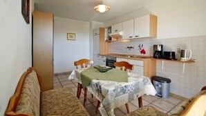 Une cuisine compacte avec des meubles en bois, une table à manger recouverte d’une nappe verte et une petite poubelle.