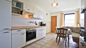 Une cuisine compacte avec des meubles blancs, un plan de travail en bois et un coin repas comprenant une table et des chaises.
