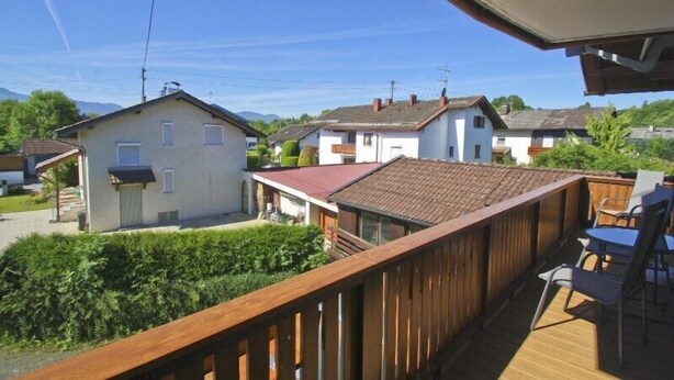 Une terrasse en bois avec des sièges extérieurs, offrant une vue sur un quartier résidentiel avec des maisons et de la verdure.