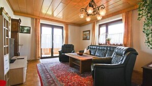 Un salon avec un plafond en bois, un canapé en cuir noir, une table basse en bois et un tapis rouge à motifs.