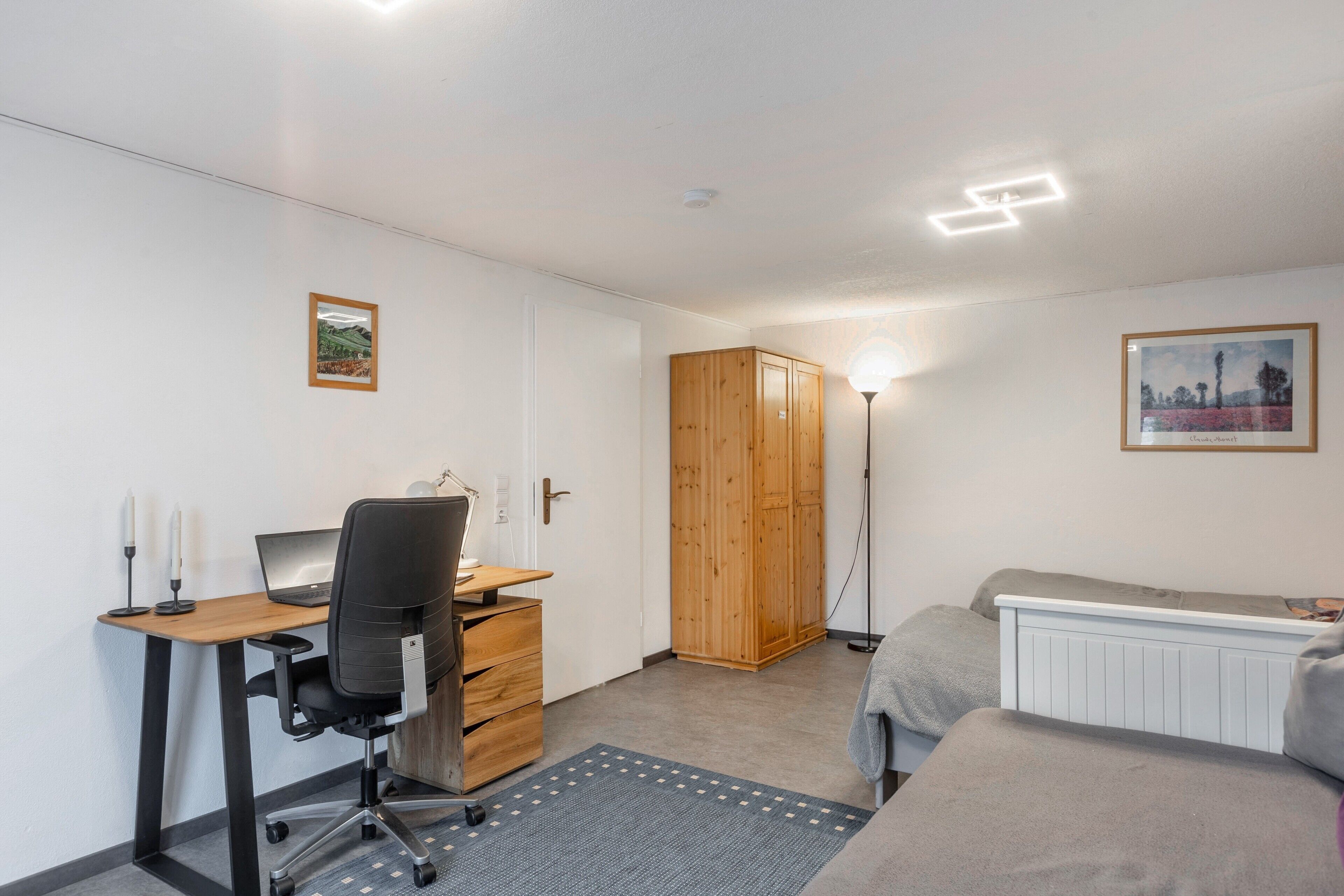Une chambre à coucher avec un lit, un bureau avec un ordinateur portable, une armoire et un radiateur.