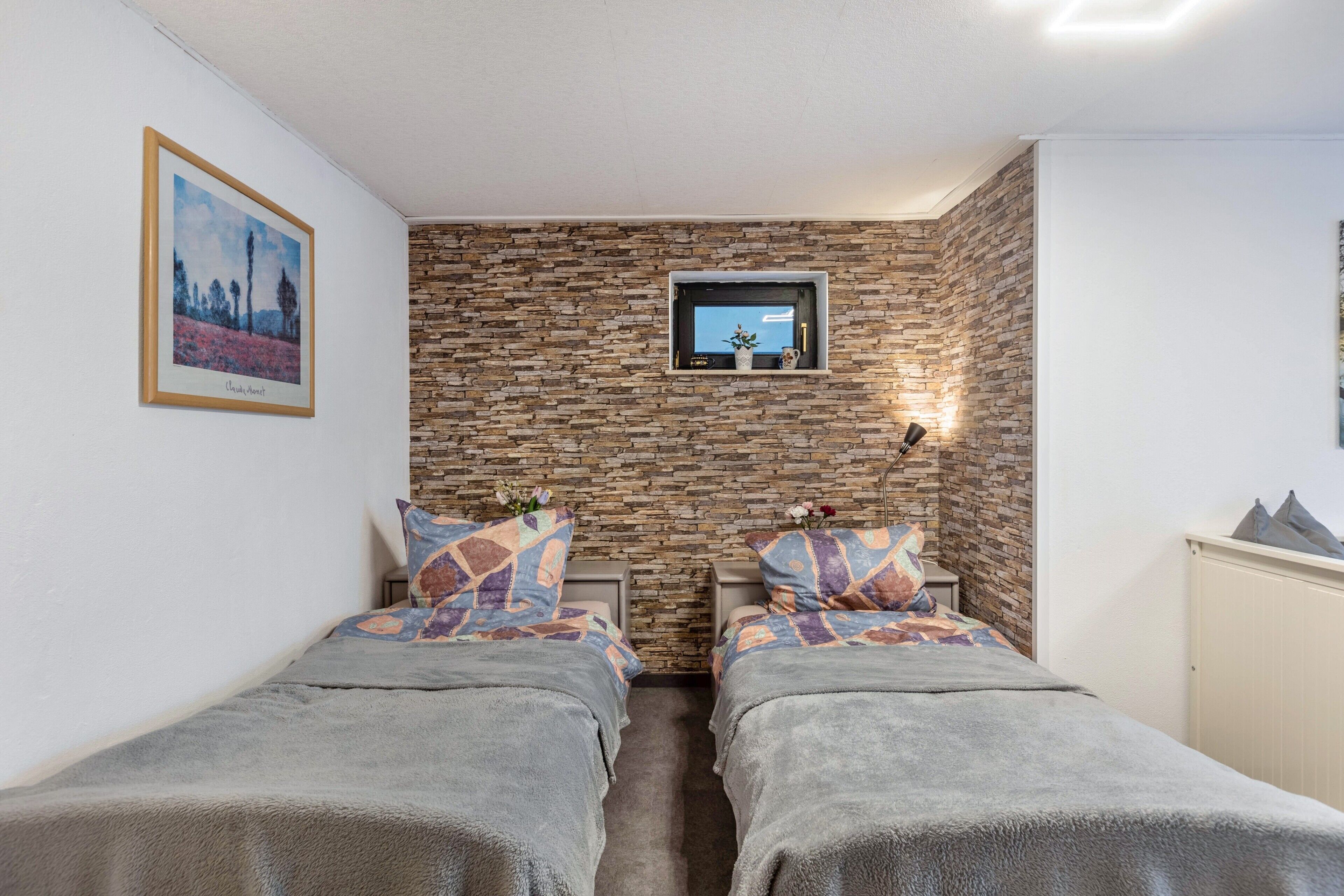 Ein Zimmer mit zwei Betten, einer Steinsäule, einem Fernseher und einem gerahmten Bild.