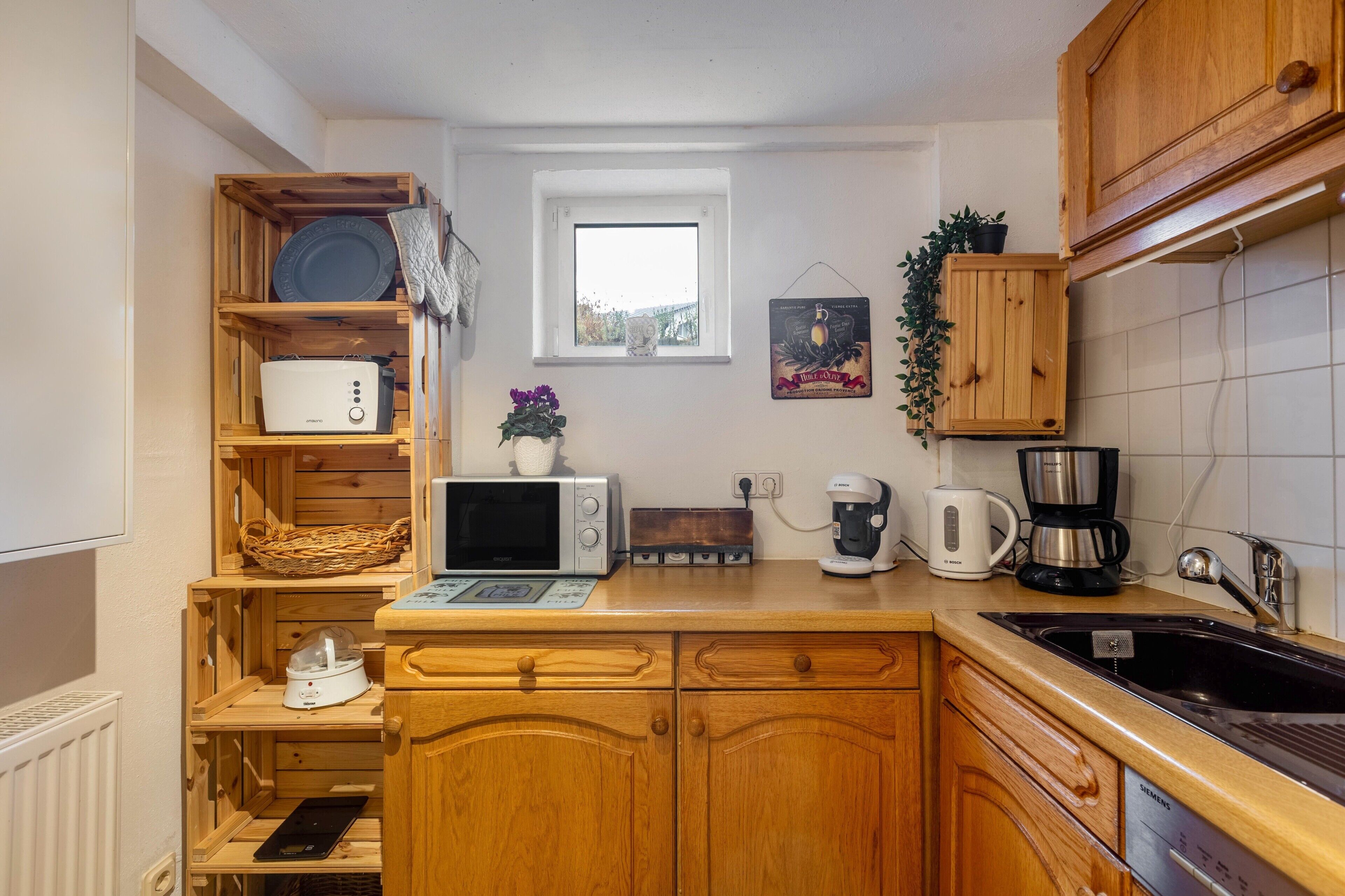 Una cocina compacta con armarios de madera, un microondas, un tostador, una cafetera y una ventana pequeña.