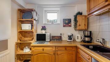 Una cocina compacta con armarios de madera, un microondas, un tostador, una cafetera y una ventana pequeña.