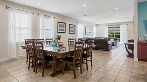A spacious living room with a glass-top dining table surrounded by wooden chairs, a sofa, and a coffee table.