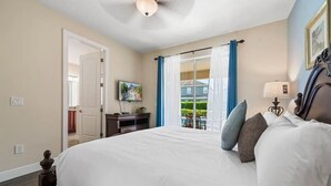 A hotel room with a large bed, a desk, a television, and a view of the outside balcony.