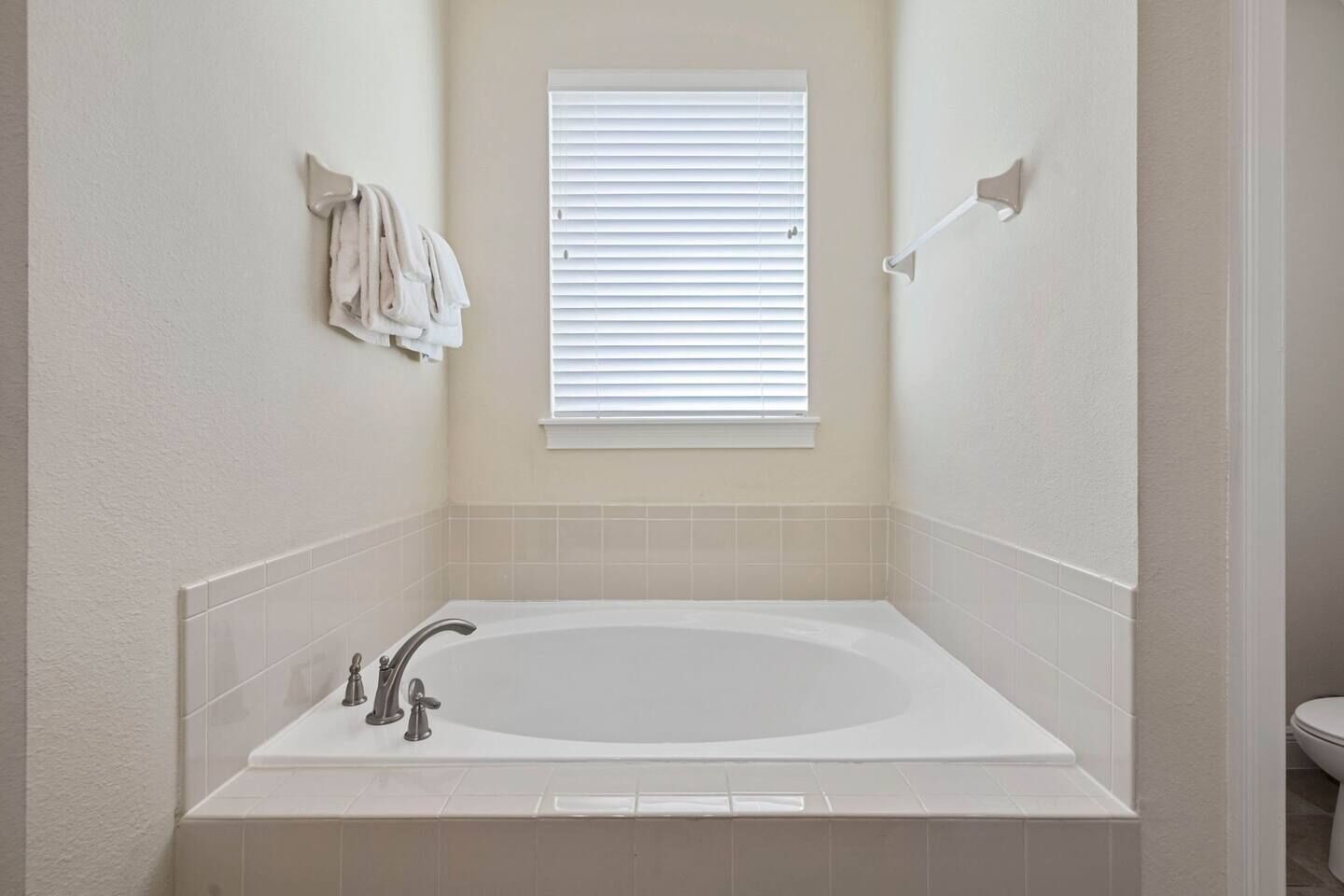 A bathroom with a large bathtub, a window with blinds, and a towel rack.