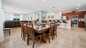 A spacious kitchen with modern appliances, a dining area with wooden chairs, and a living area with a sofa and TV.