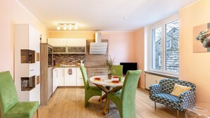 Een moderne keuken met witte kasten, een betegelde achterwand en een eethoek met groene stoelen en een ronde tafel.