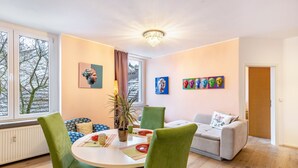 Een kamer met een eettafel, groene stoelen, een bank en kunstwerken aan de muur.