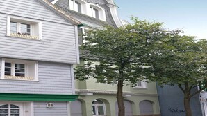 Een gebouw met twee verdiepingen, een groen dakoverhang, een boom ervoor en een stenen muur.