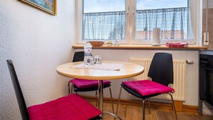 A room with a round table, two chairs, a radiator, a window with a view, and a painting on the wall. - Apartment 'Haus Grete' with Lake View and Balcony (Langenargen)