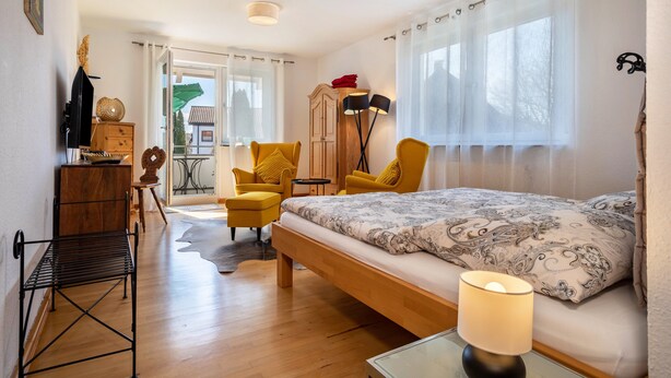 A bedroom with a bed, two chairs, a desk, a wardrobe, and a window with curtains. - Apartment 'Haus Grete' with Lake View and Balcony (Langenargen)