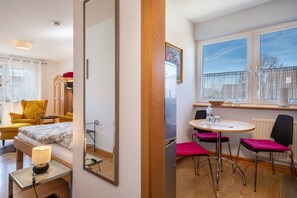 Una habitación de hotel con una cama, un escritorio con lámpara, un área de comedor con mesa y sillas, y un ventanal con vistas.