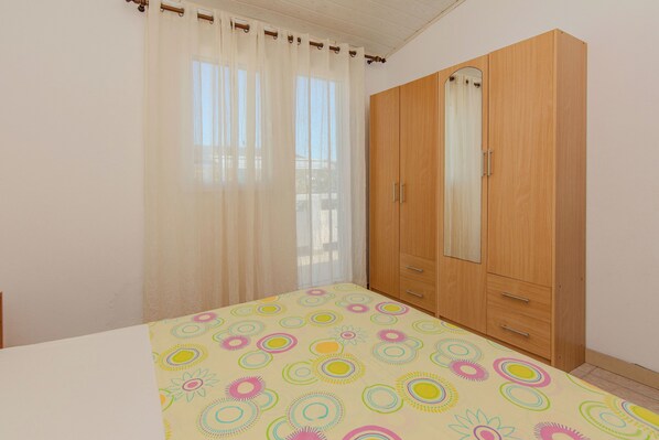 A bedroom with a bed, a wardrobe, and a window with sheer curtains.