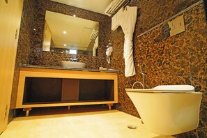 Baño con pared de mármol, lavamanos, espejo, bañera y toallero.