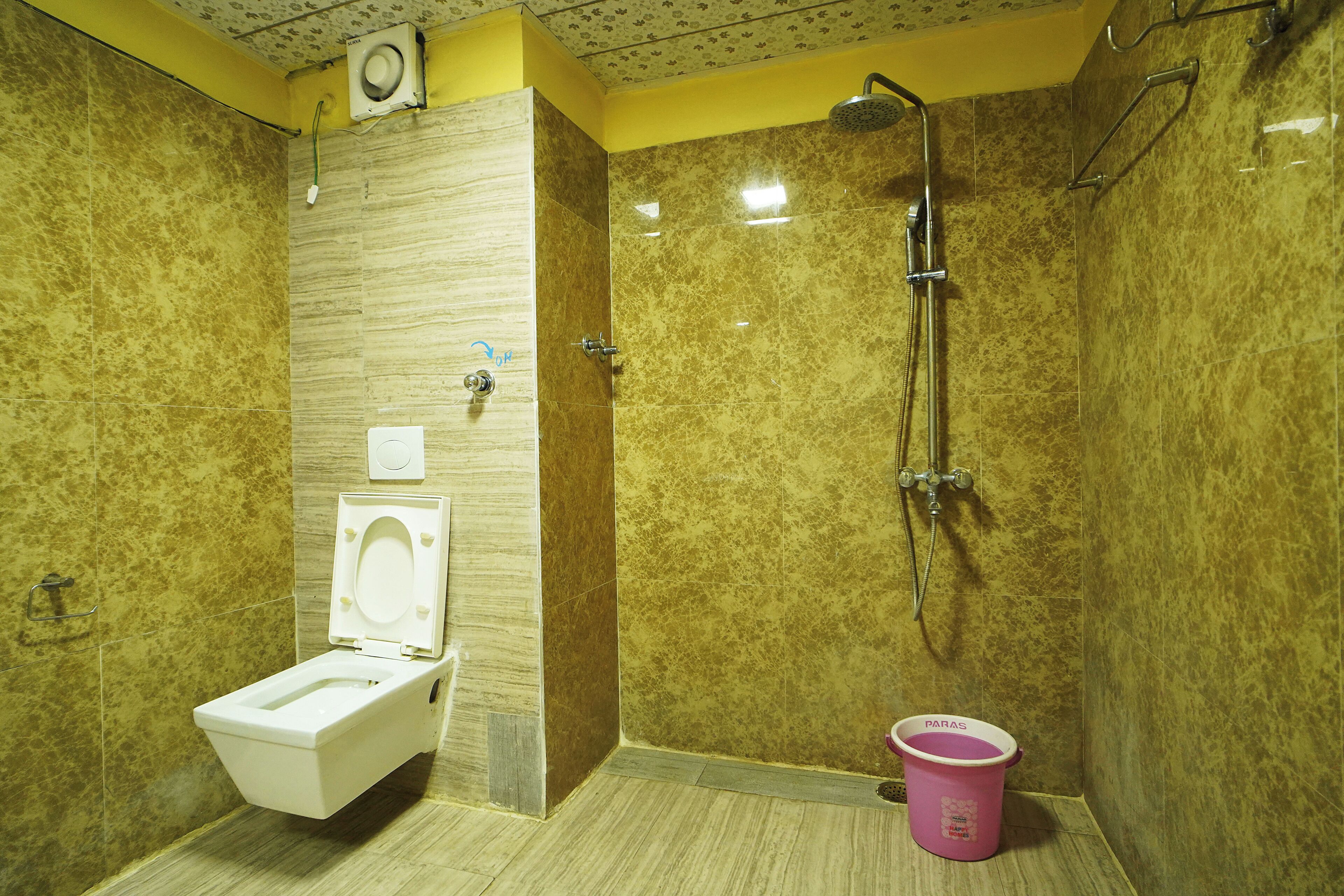 A bathroom with a toilet, shower, and a pink bucket.