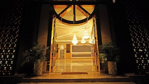 Entrada de hotel con diseño moderno, que incluye una recepción, candelabros y plantas en macetas.