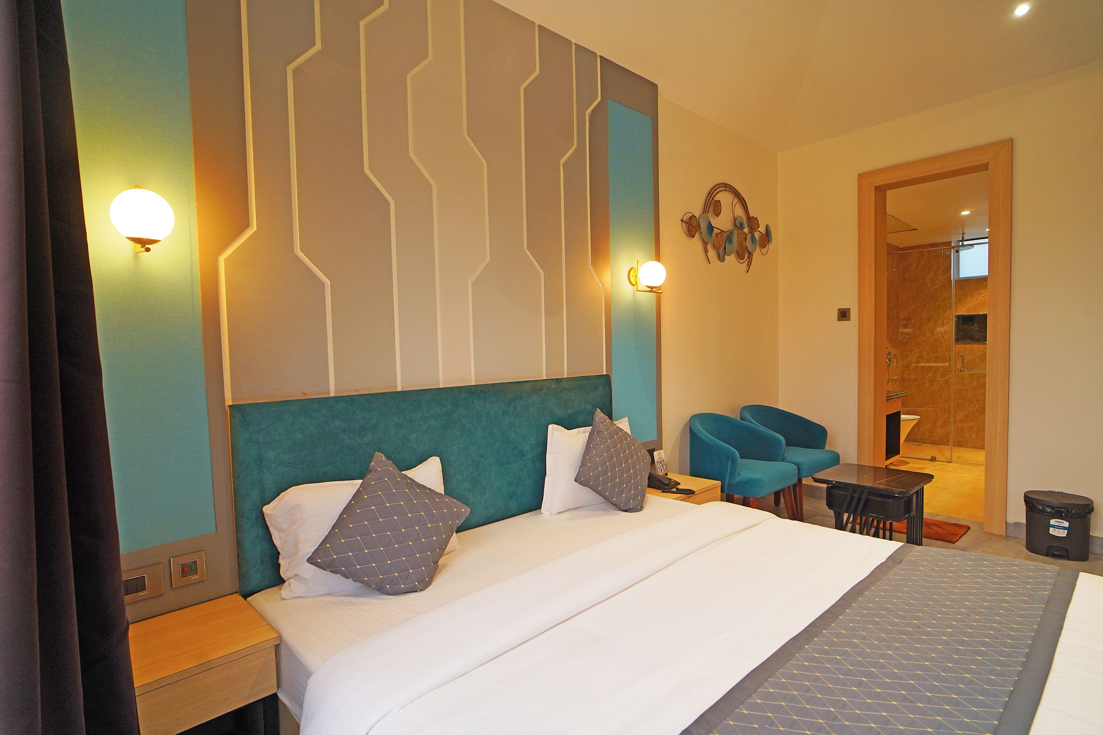 Une chambre d’hôtel avec un lit, des tables de chevet, un bureau, une chaise et une salle de bain visible à travers une porte ouverte.