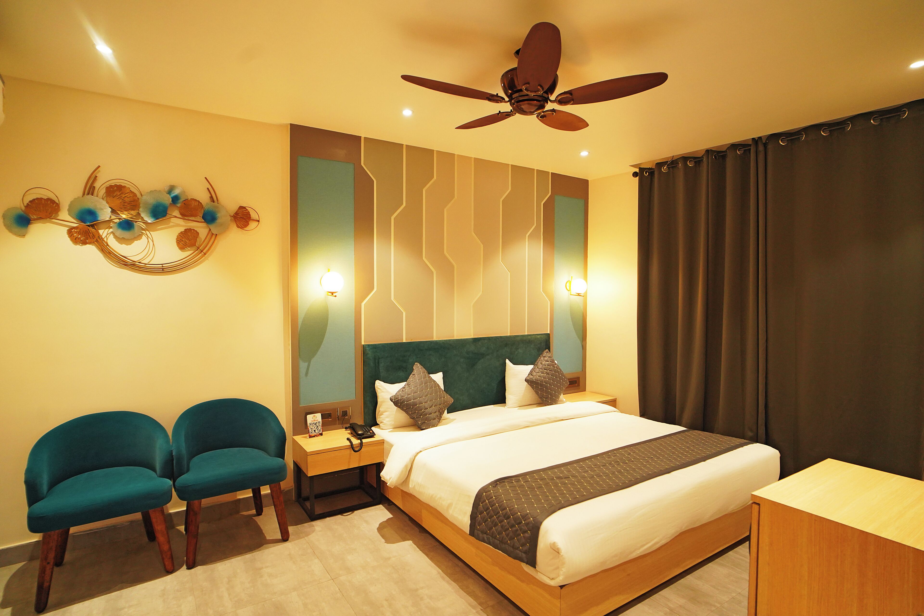 Une chambre d’hôtel comprenant un lit, deux chaises, un ventilateur de plafond et un mur agrémenté d’éléments décoratifs.