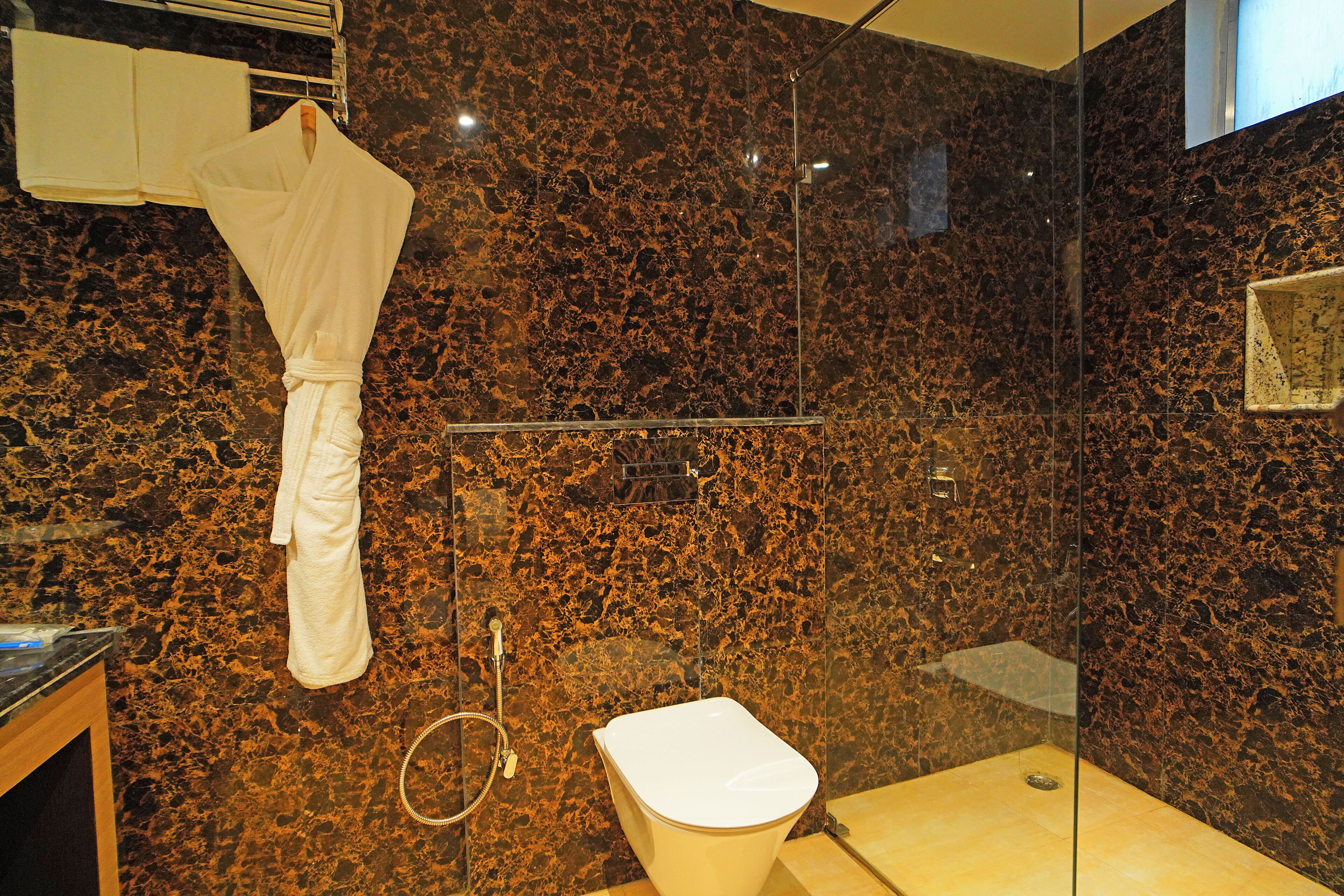 Un baño con cabina de ducha de vidrio, una bañera blanca y una bata colgada en un perchero.