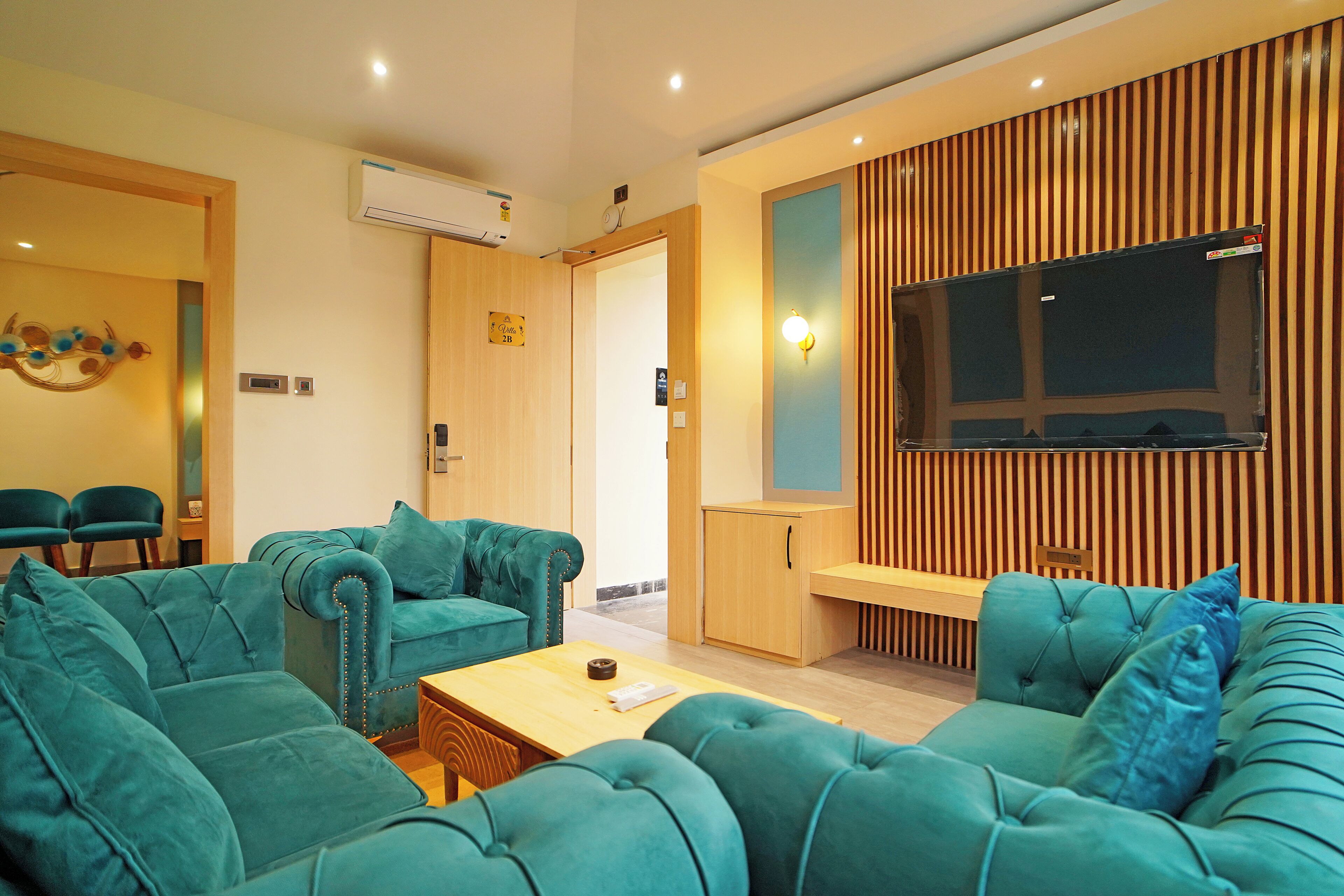 Una sala de estar moderna con sofás color turquesa, un mueble de madera y un televisor de pantalla plana montado en una pared de paneles de madera.