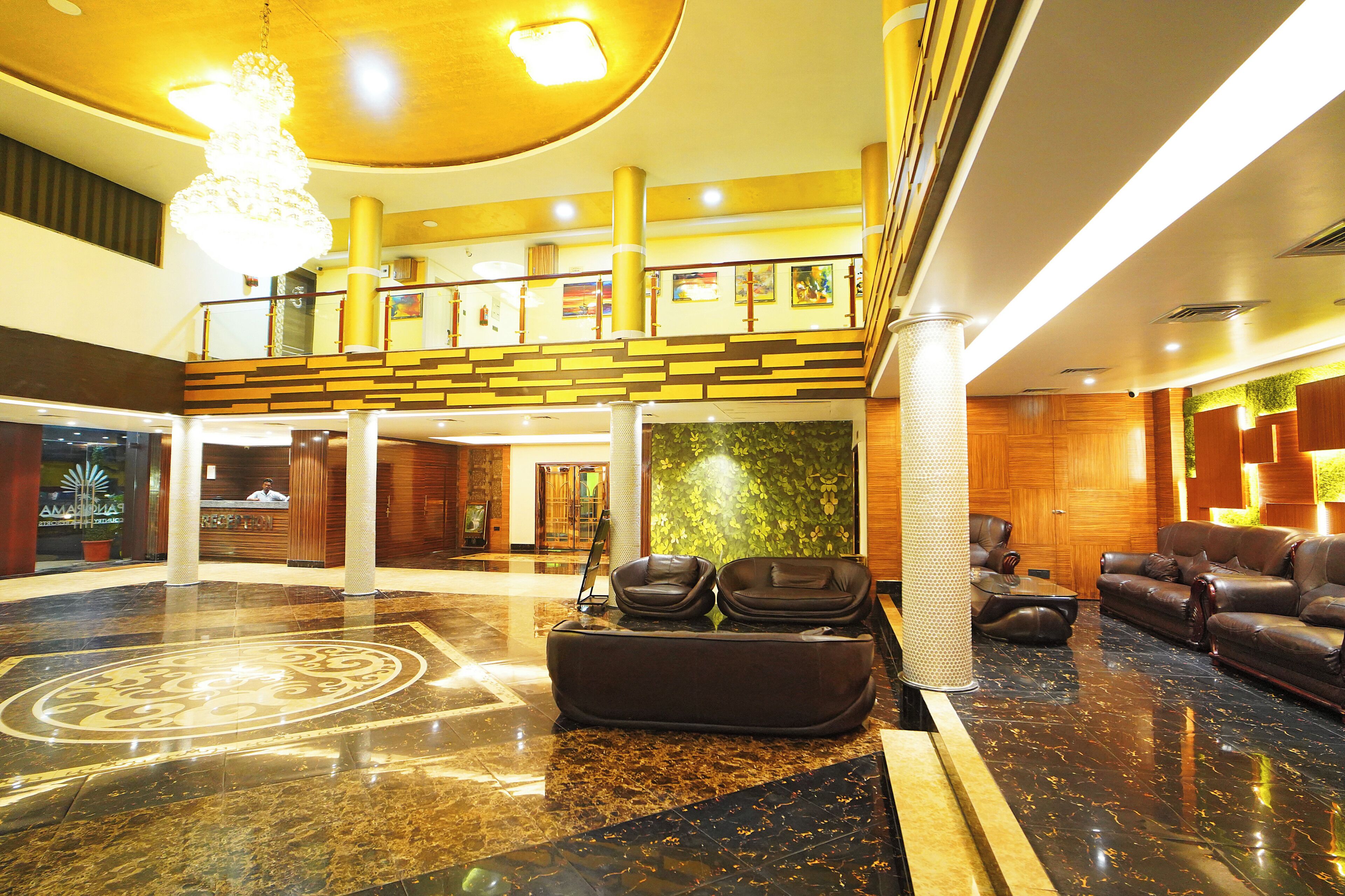 A lobby with a reception desk, a seating area with leather sofas, a chandelier, and a decorative floor pattern.