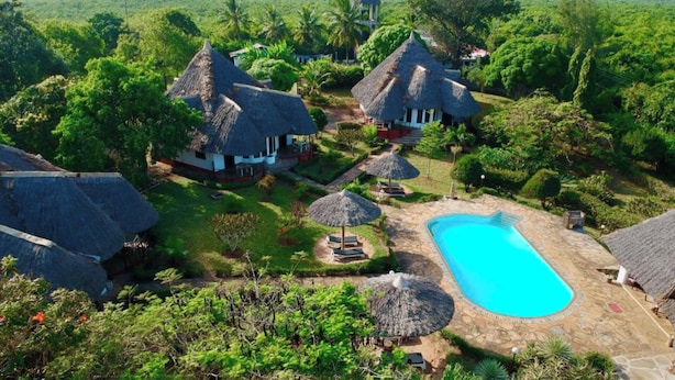 Un complexe hôtelier doté de bungalows aux toits de chaume, d’une piscine et d’une végétation luxuriante.