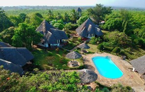 A resort with thatched-roof cottages, a swimming pool, and lush greenery.