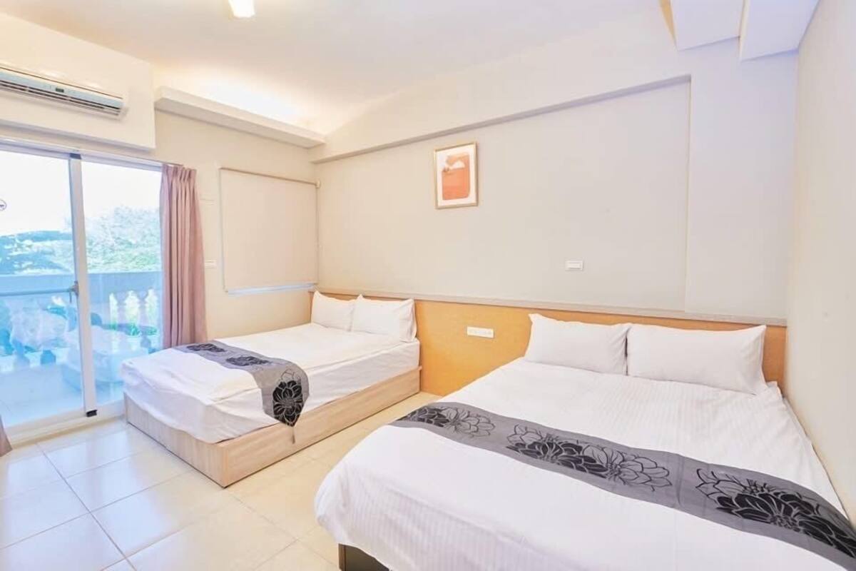 A hotel room with two beds, a large window with a view, and a sliding door to a balcony.