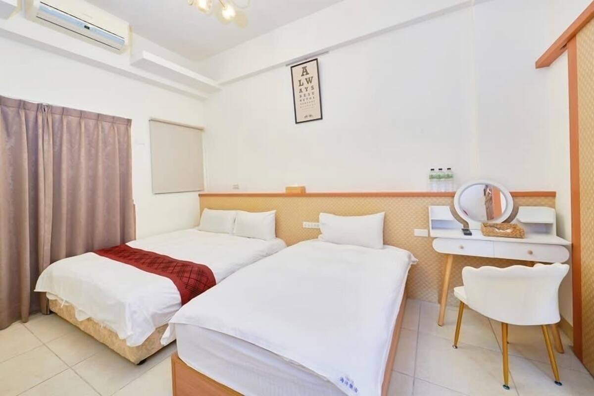 A hotel room with two beds, a desk with a mirror, and a wall-mounted air conditioning unit.