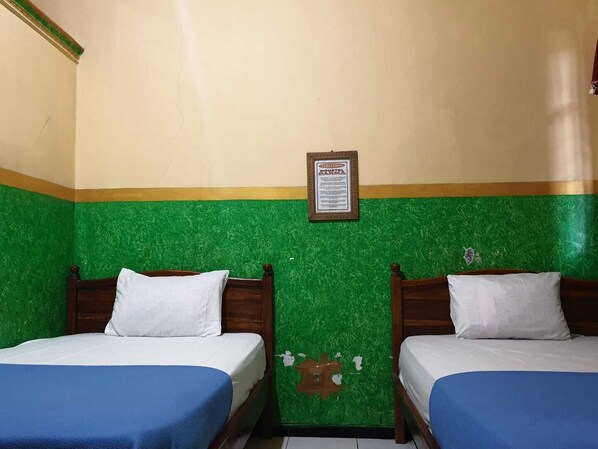 Una habitación con dos camas, cada una con colcha azul y almohadas blancas, y una pared verde con un cartel.