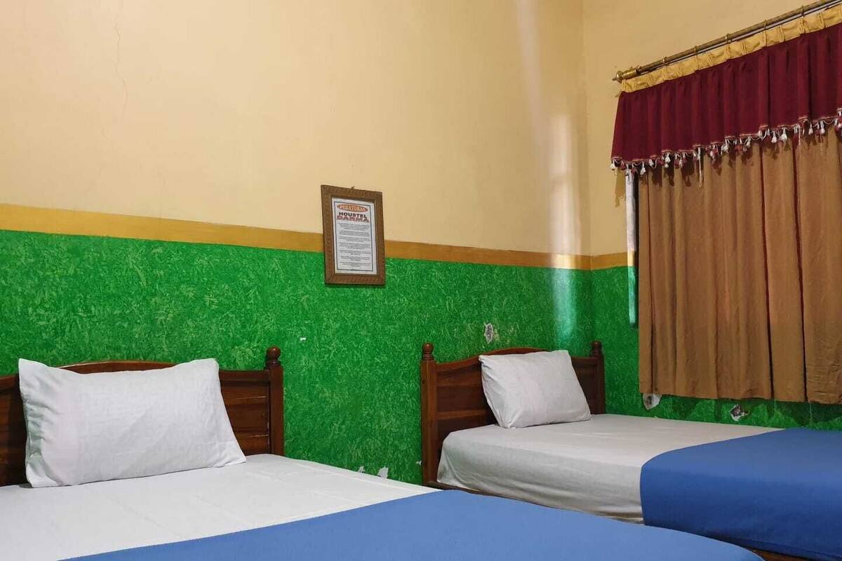 A room with two beds, green walls, a framed sign on the wall, and a curtain.