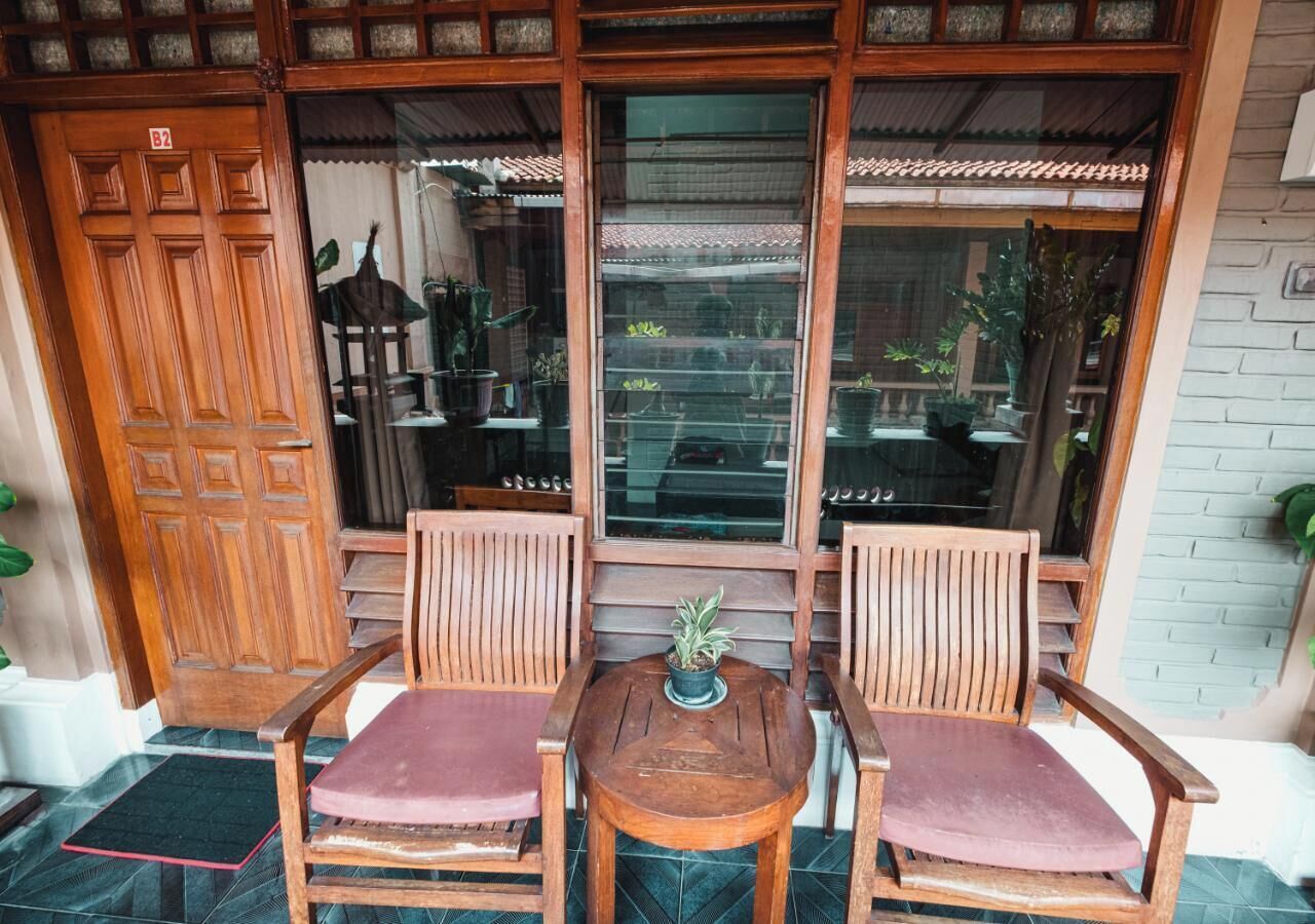 A wooden porch with two chairs and a table, a wooden door, and a window with a view of the garden.